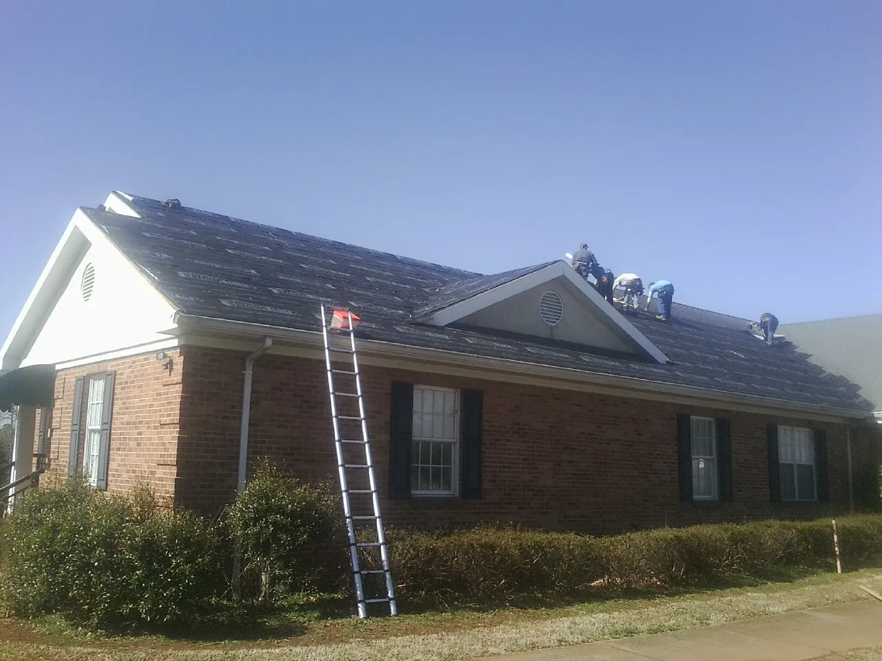 Crew tearing shingles off a brick ranch roof with a ladder set — Emergency Roof Repair work by our crew in Delco