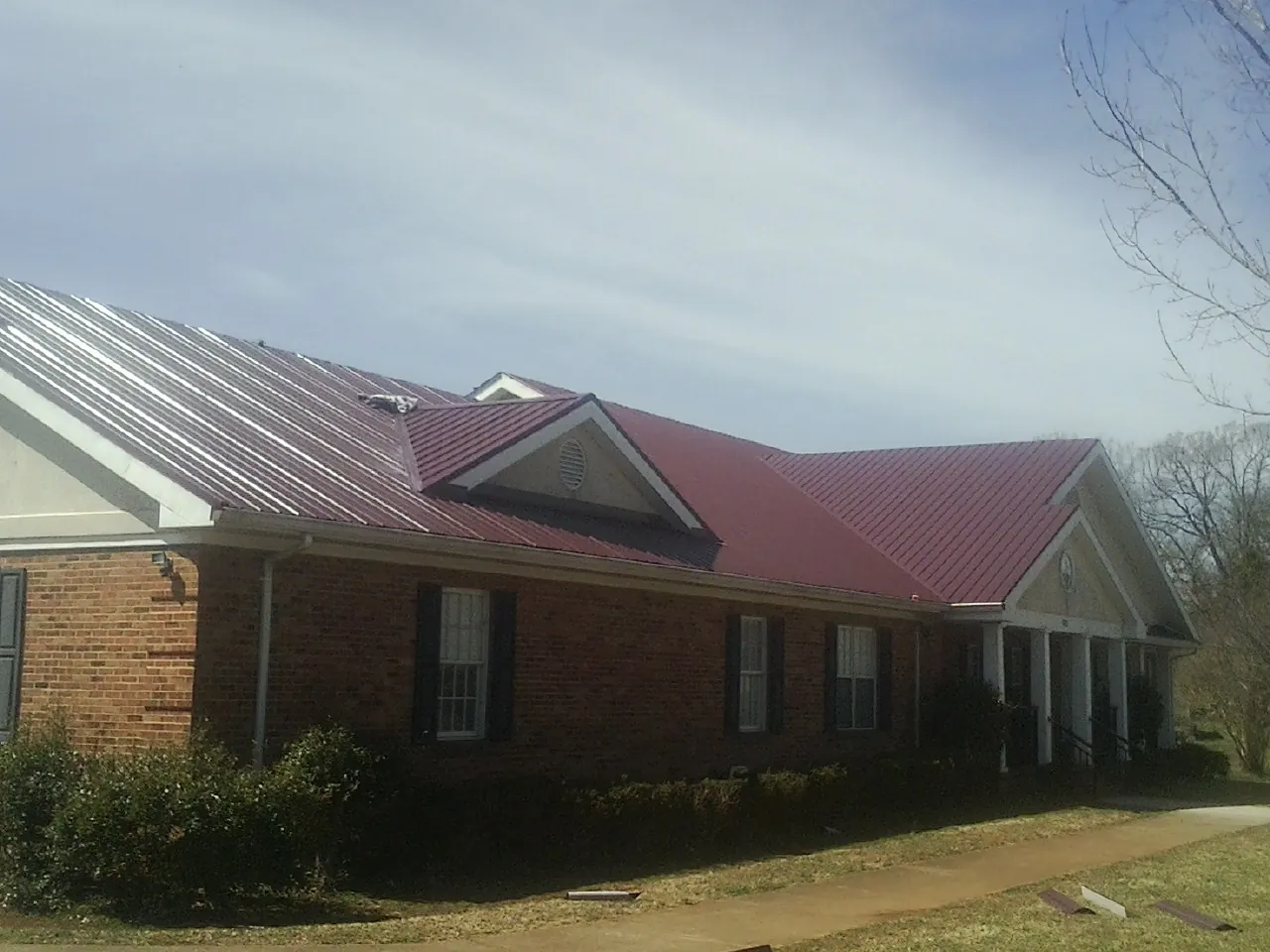 Red metal roof with gabled entries on a long brick building, from a Hail Damage Roof Repair job in Delco