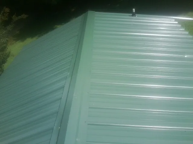 New green metal panels meeting at the ridge of a roof — Flat Roof Repair work by our crew in Delco