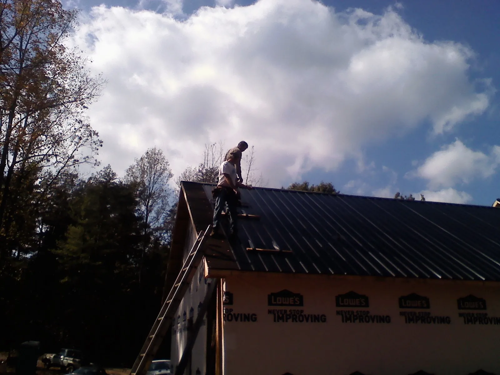 Roofer fastening dark metal panels high against a cloudy sky, from a Roof Inspection job in Delco